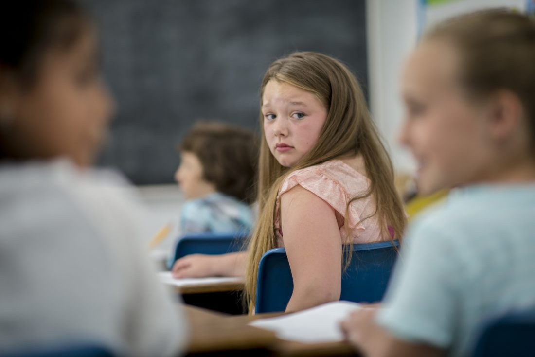 Menina em sala de aula observando a conversa de outros colegas 