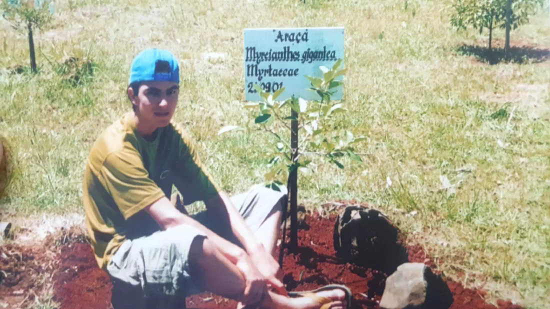 Menino sentado no chão, plantando árvore no bosque da EEB General Liberatto Bittencourt, em Itá