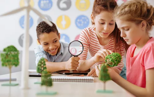 Alunos segurando lupa examinando modelo de árvore em sala de aula aprendendo com método conhecido como abordagem investigativa
