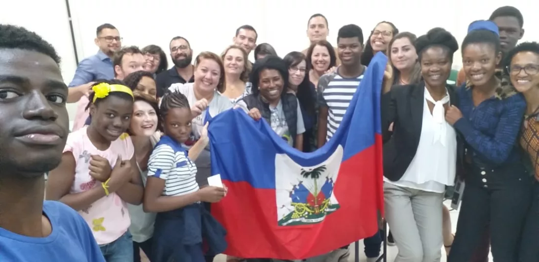 alunos imigrantes segurando uma bandeira do Haiti em sala de aula em projeto "Abraços Abertos" da EEB Professora Maria Amin Ghanem, de Joinville 
