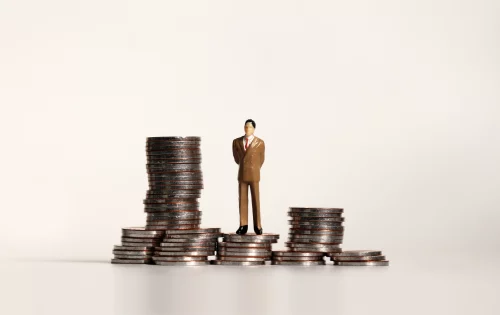 Boneco sobre pilha de moedas representando o sistema Capitalista