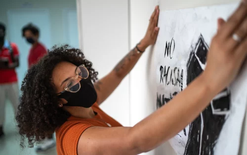 Mulher afrodescendente colando um cartaz antirracista na parede de uma escola que trabalha com a educação antirracista