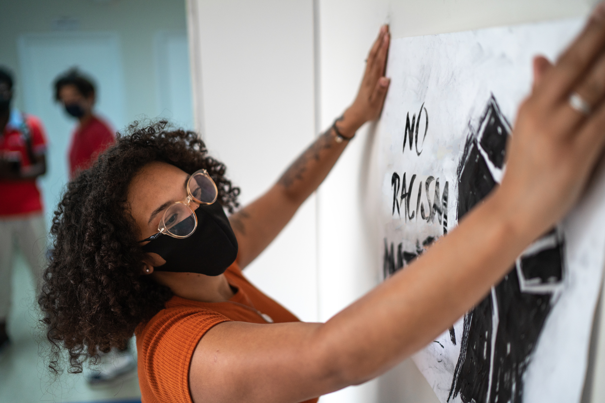 Mulher afrodescendente colando um cartaz antirracista na parede de uma escola que trabalha com a educação antirracista 