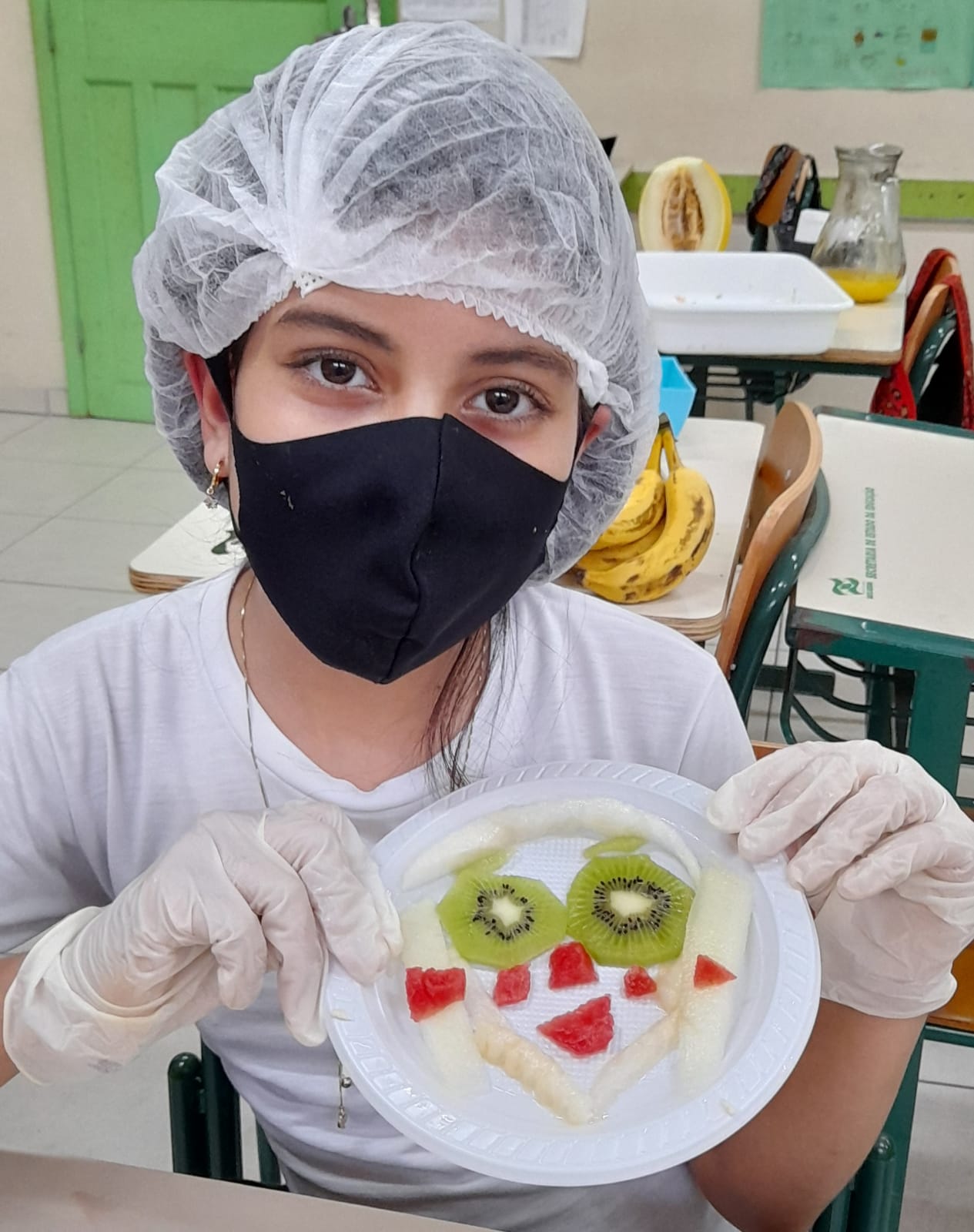 estudante mostra rosto feito com frutas kiwi, melancia e banana no projeto de educação alimentar e nutricional