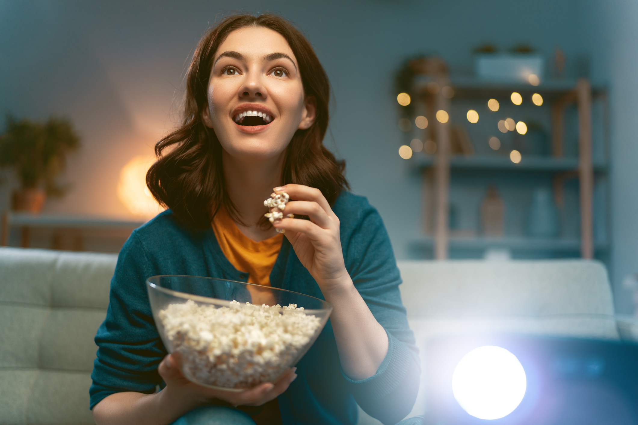 Mulher sentada no sofá ao lado de um projetor cinematográfico, comendo pipoca, assistindo filmes sobre educação inclusiva 