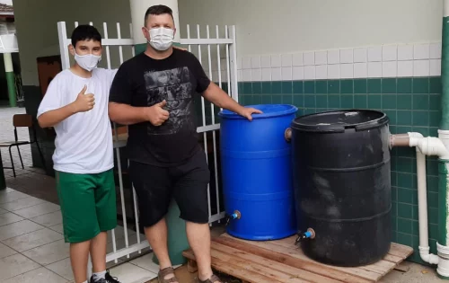 George Willian Wulf e o filho, Kaio Yan Wulf, aluno do sexto ano matutino da EEB Engenheiro Annes Gualberto, ao lado de cisterna instalada no pátio da escola de São Francisco do Sul