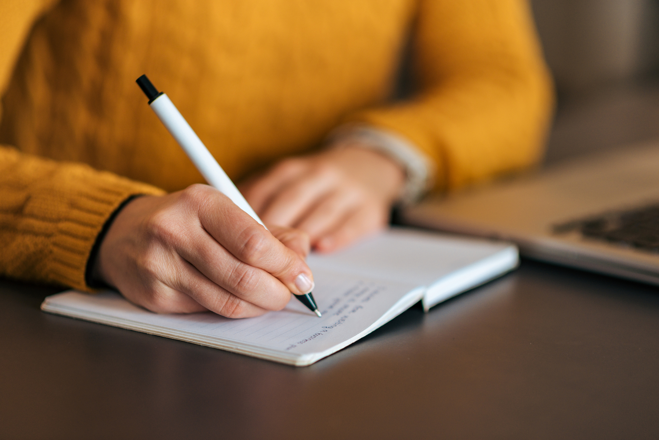 Imagem mostra uma mão segurando uma caneta fazendo anotações em um caderno