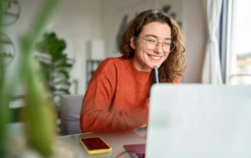 Imagem mostra estudante em frente ao computador sorrindo