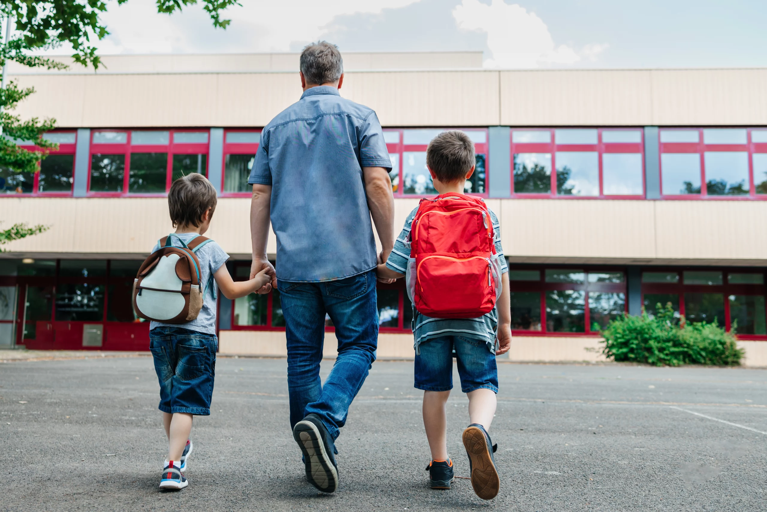 imagem mostra pai de mãos dadas com dois filhos chegando na escola