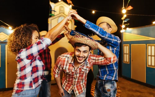 Imagem mostra três jovens com trajes típicos de festa junina dançando quadrilha