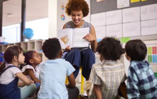 Professora lê para alunos de escolas primárias multiculturais sentados no chão em sala de aula na escola